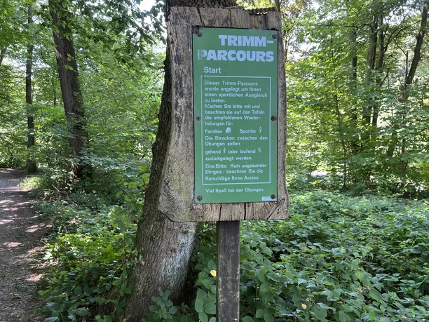 Fitness pad Een houten bord in het bos markeert het begin van een fitnessroute met een groen informatiepaneel.