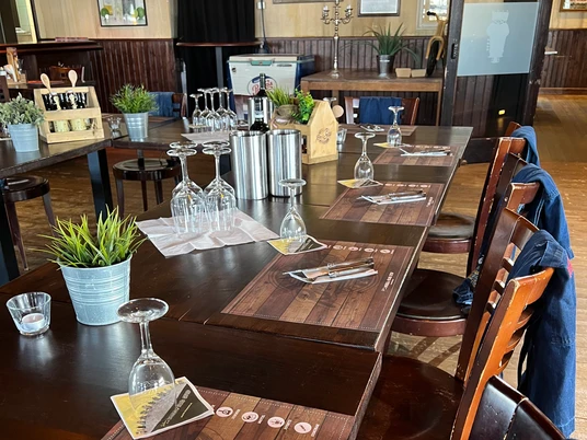 Corso di grigliata al Road Stop Mettmann Un tavolo di legno apparecchiato a festa con bicchieri da vino e tovagliette in una sala da pranzo rustica.