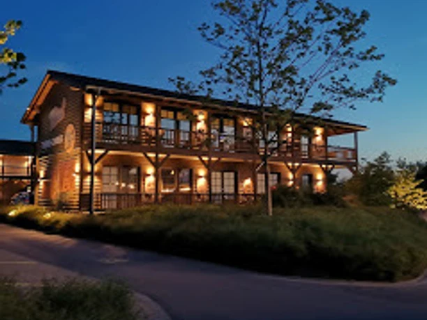 Hotel Road Stop Mettmann bei Nacht Beleuchtetes Hotelgebäude in Mettmann, umgeben von Pflanzen bei Dämmerung, darunter ein großer Baum.