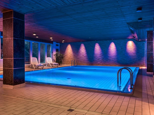 Piscine de l'hôtel am Stadtpark, Hilden Piscine intérieure de l'hôtel am Stadtpark Hilden, illuminée de manière atmosphérique avec des lumières bleues et violettes.