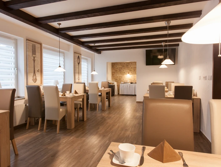 Hotel Angerland, Ratingen'deki kahvaltı salonu Ahşap masalar, bej sandalyeler ve sarkıt aydınlatmalarla samimi bir atmosfer yaratan bir kahvaltı odası.