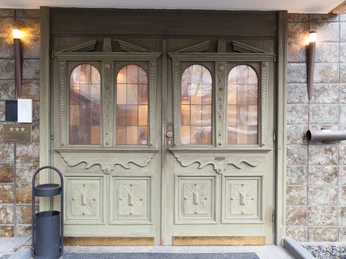 Ratingen'deki Hotel Angerland'ın giriş kapısı Süslü vitray pencerelere sahip devasa ahşap bir kapı, zarif bir otele açılıyor. Girişte lambalar vurgulanıyor.