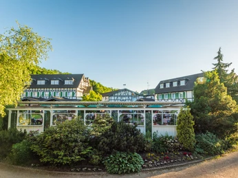 Lohmann's Romantik Hotel Gravenberg in Langenfeld An elegant half-timbered hotel surrounded by lush greenery under a bright blue sky.