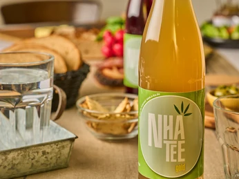 Kraliyet NHA kenevir çayı Yeşil etiketli altın renkli bir şişe kenevir çayı, atıştırmalıklarla donatılmış bir masanın üzerinde duruyor.