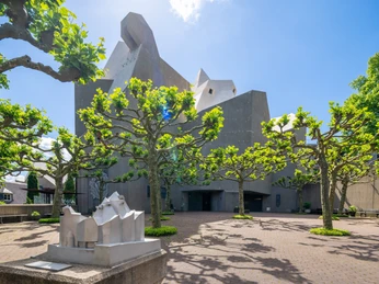 Statua di Neviges Mariendom Moderno edificio in cemento della Cattedrale di Neviges, con iconiche forme geometriche, circondato da alberi.