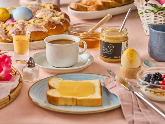 Frühstück im neanderland au miel de Düssel Un petit-déjeuner varié avec une tranche de pain grillé et du miel de Düssel, entouré de pâtisseries de Pâques et de café.