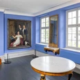Cromford Brügelmannów Jasny pokój z niebieskimi ścianami, drewnianym zegarem, obrazami, lustrem i okrągłym stołem.