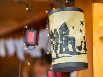 Latarnia na targu św. Marcina w Monheim Artystycznie zaprojektowana latarnia z motywami wyciętymi z papieru emanuje ciepłym światłem nad straganem na targu.