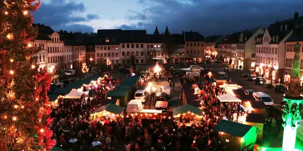 Blick auf die Verkaufstände des hell erleuchteten Weihnachtsmarkts auf dem Marktplatz in Rochlitz am Abend