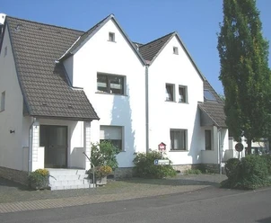 Vakantieappartement Kemper Een wit huis met twee verdiepingen, vier puntgevels, grijze daken en een goed onderhouden voortuin.