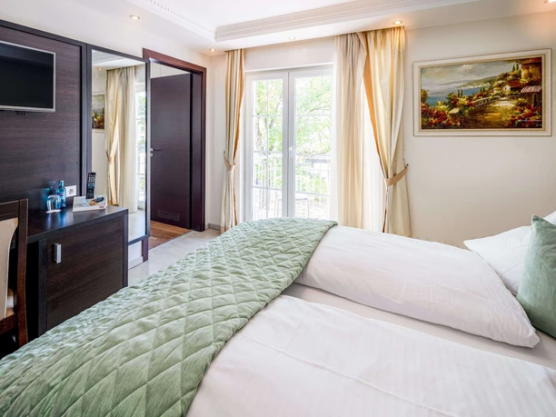 Balkonlu Oda Kristallhotel FETTEHENNE Çift kişilik yatak, çalışma masası, TV, balkon erişimi ve aydınlık iç tasarıma sahip geniş otel odası.