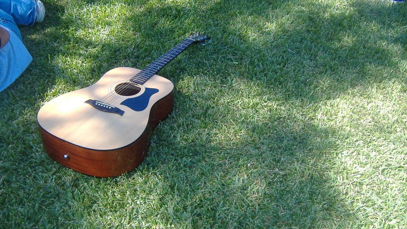 Akustische Gitarre liegt auf grünem Gras, umgeben von Personen, von denen nur Beine sichtbar sind