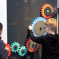 Chain reaction for families Two children interact with colorful gears on a blackboard, which represents an experimental field.