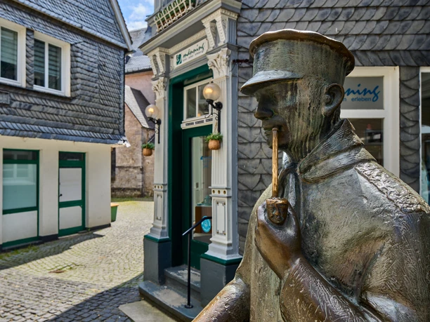 Centre-ville historique de Wülfrath Une statue en bronze d'un homme fumant la pipe se dresse devant des maisons à colombages au toit d'ardoise à Wülfrath.