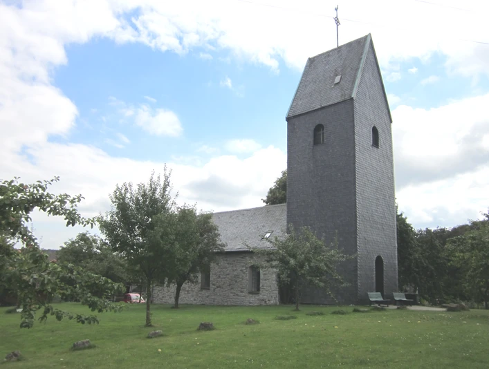 Kaplica Windrath, Velbert Zabytkowa kaplica w Velbert z kamienną wieżą otoczoną zielonymi łąkami i drzewami.