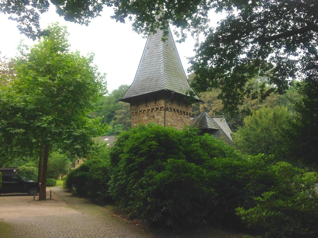 Zamek Caspersbroich z zewnątrz (własność prywatna) Zamek Caspersbroich w Solingen, z jego wieżami i bujną zielenią, wznosi się pośród gęstej roślinności.