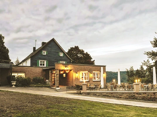 Restauracja Op dä Höh w Hattingen Restauracja w ceglanym budynku z tarasem, drzewami i zachmurzonym niebem w tle.
