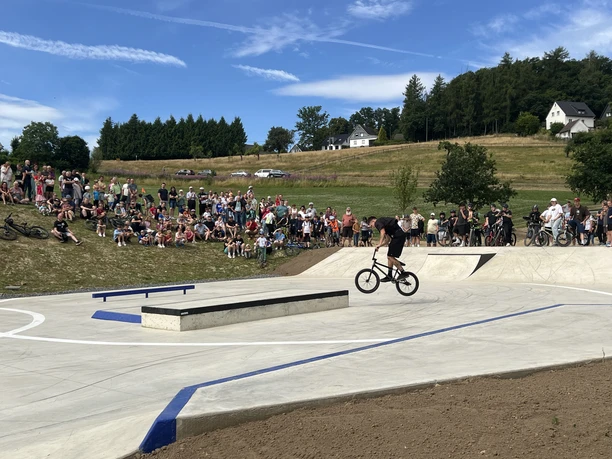 Waldbröl Skate- en Bikepark Een grote groep mensen kijkt naar BMX-rijders op een betonnen skatepark met op de achtergrond een groen landschap.