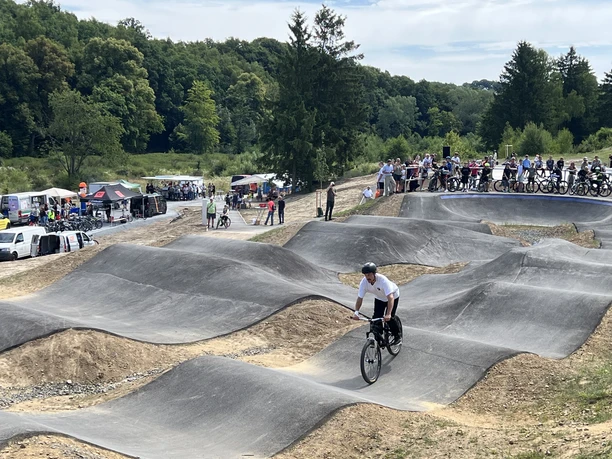 Waldbröl Skate- en Bikepark Een BMX-rijder beheerst bochten op een hobbelige asfaltbaan, omringd door toeschouwers in de openlucht.