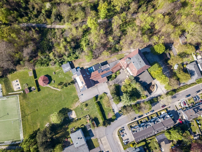 The grounds of the Velbert Youth Hostel from above Aerial view of the Velbert youth hostel, surrounded by greenery, near a sports field and a road.