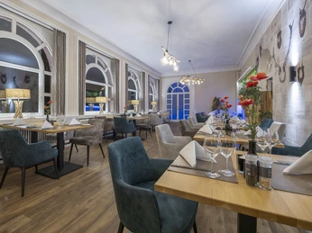 Jadalnia w restauracji Blattwerk w Fletcher Hotel-Restaurant Waldhotel Nadrenia Północna-Westfalia Jadalnia w restauracji Blattwerk z ustawionymi stołami, zielono-niebieskimi krzesłami i dużymi oknami.