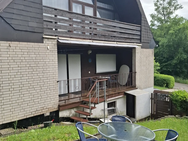 Balkonappartement 1 en 2 Achteraanzicht van een twee verdiepingen tellend huis met balkon, terras, heg en ronde zithoek in de tuin.