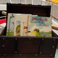 Journée nationale de la lecture Un coffre en bois rempli de livres pour enfants, dont « Janosch : Petit Lapin, Grand Héros », sur une table.