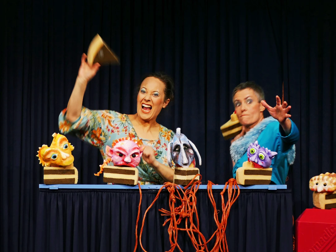 Blazing rage Two puppeteers animate colorful, imaginative puppets on a small stage with a curtain.