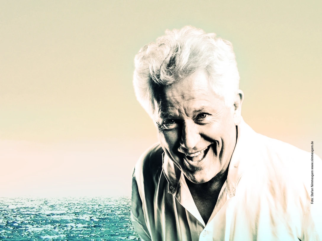 Alexis Zorba Gün batımında, uçsuz bucaksız, yumuşak ışıklı bir okyanusun önünde gülümseyen yaşlı bir adamın portresi.