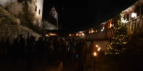 Es ist bereits dunkel draußen und der Wehrgang von Schloss Rochsburg ist mit Fackeln beleuchtet.