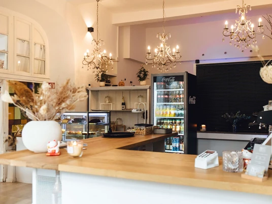 Il Neandertal n. 1 - Caffè ed eventi a Erkrath Un caffè luminoso con lampadari, banconi in legno e vetrine refrigerate che emana un'atmosfera calda.