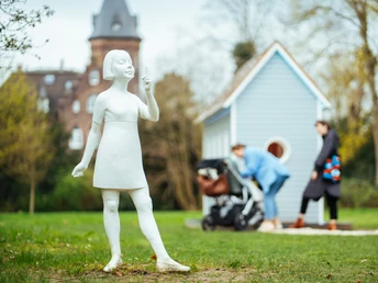 Opera d'arte "Sì, non c'è dove" nel Marienburgpark Opera d'arte "Yes There No Where" di Robert Wilson nel parco di Marienburg, Monheim. Una piccola casa blu e una scultura bianca circondate da un prato verde. Sullo sfondo si vede il castello di Marienburg. Genitori con passeggini osservano la casa.