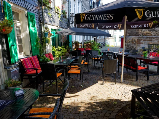 Birreria all'aperto, Dingle's Irish Pub a Mettmann Una birreria all'aperto con tavoli in legno scuro e cuscini rossi sotto gli ombrelloni della Guinness.