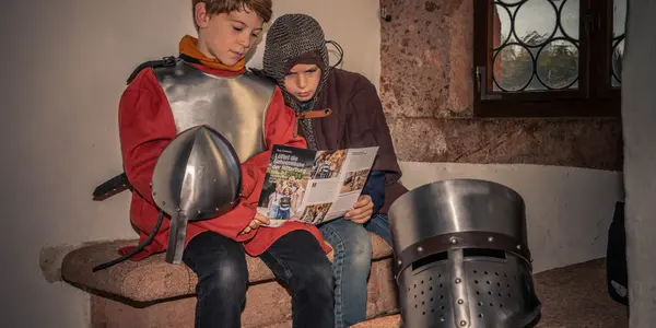 Zwei Jungen sind wie Ritter angezogen und schauen sich einen Prospekt über die Burg Kriebstein an.