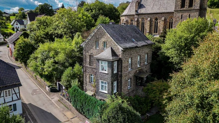 Catholic Parish House Catholic parish house made of stone with bay window and slate roof, surrounded by trees and a church.