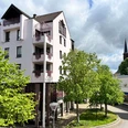 Ferienwohnung Der Gerber in Hilden Mehrstöckiges helles Gebäude mit Balkonen und grünen Bäumen in Hilden, im Hintergrund ein Kirchturm.