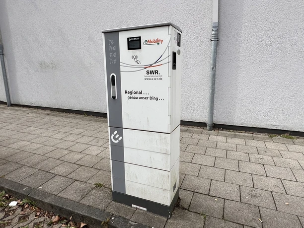 Electric vehicle charging station at the town hall square Standing electric vehicle charging station on a paved sidewalk in front of a light-colored building wall