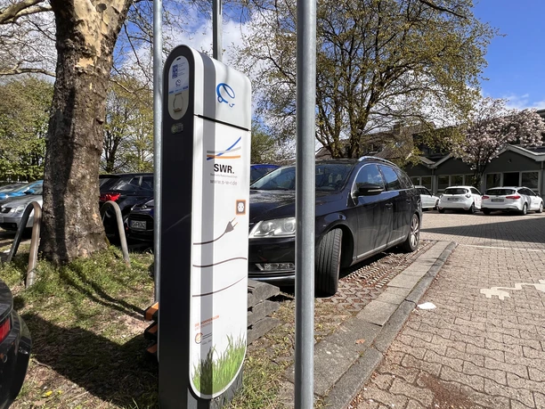 Electric vehicle charging station operated by the municipal utility company at the town hall square Charging station belonging to the municipal utility company in the parking lot in front of trees and parked cars.