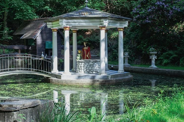 Frog King Pond Pavilion by the pond with a figure of the princess and a frog against a wooded backdrop