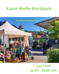 Art Mile Morsbach Marktkraam met kleurrijke gebreide kleding voor het culturele treinstation onder een blauwe hemel.