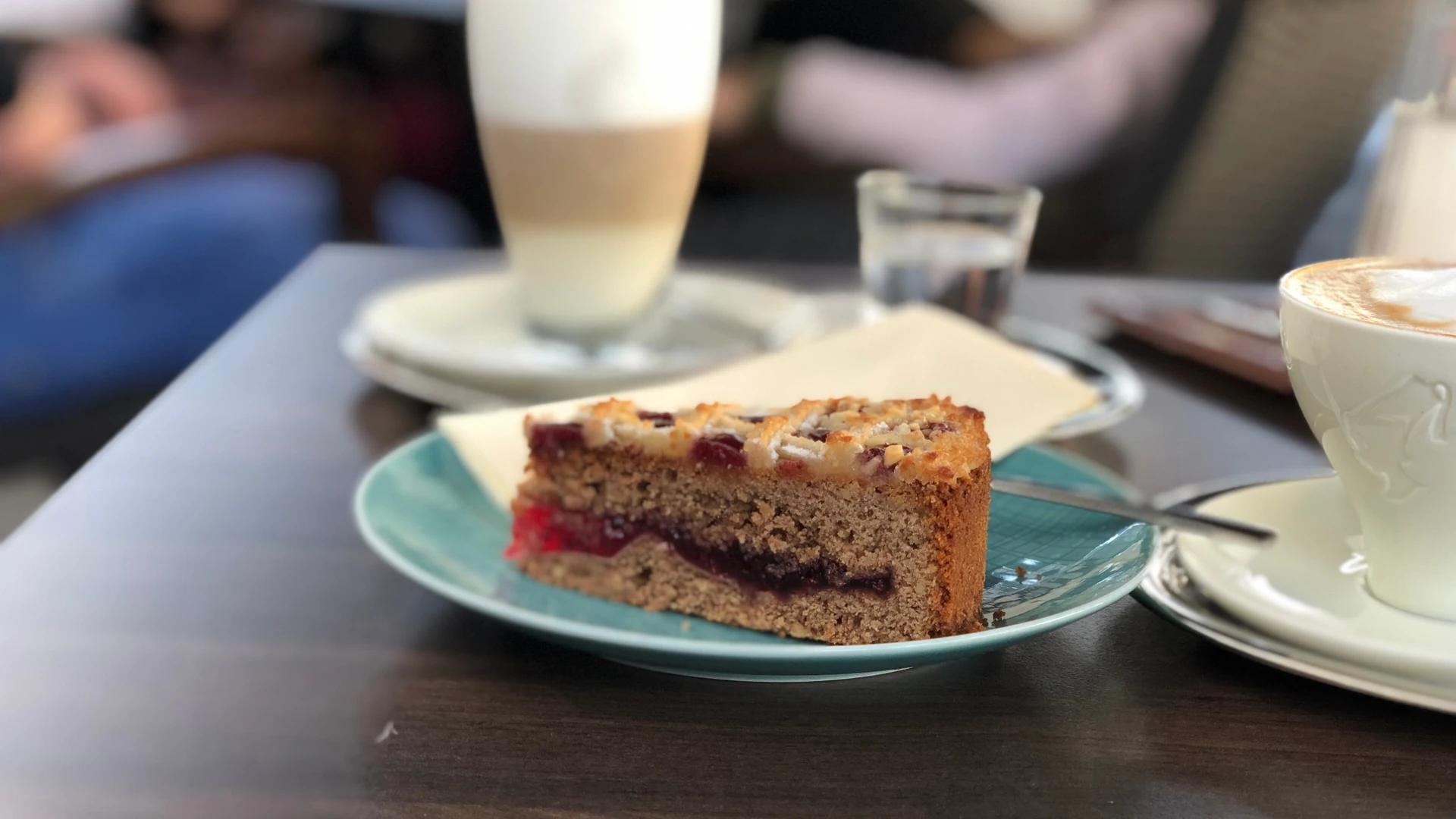 A slice of succulent cake lies on a plate next to a coffee drink in a café atmosphere.