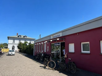 Red building of the bicycle station with parked bicycles in front of a white house under a blue sky.