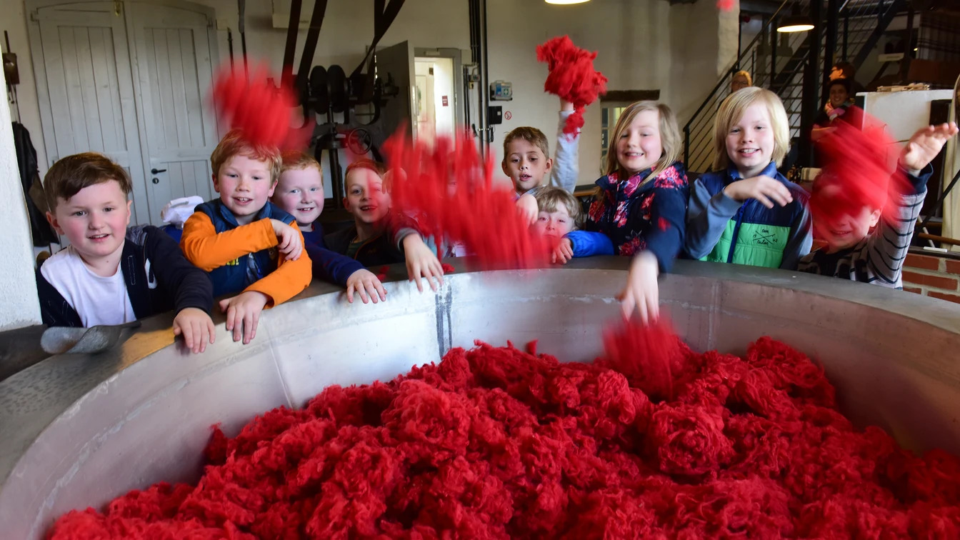 Eine Gruppe von Kindern spielt mit leuchtend rotem Baumwollflor in einem Industrieraum.
