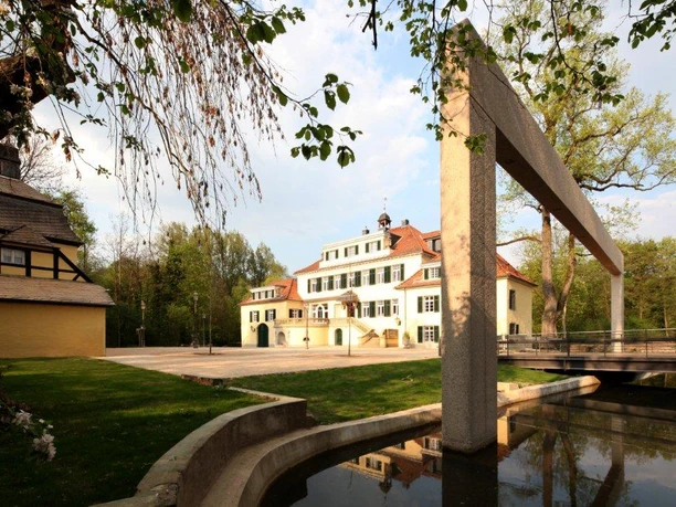 Kasteel Eulenbroich Historisch, meerlaags gebouw met een lichtgekleurde gevel, geflankeerd door moderne kunst en omgeven door bomen.