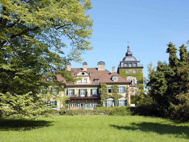 Kasteel Lerbach Historisch kasteel met torentjes en een groene gevel, omgeven door pittoreske bomen en weilanden.