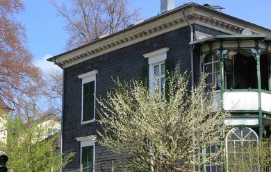 exterior view Historic building with slate facade, green shutters and balcony in a flowering environment.