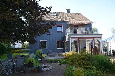 Holiday apartment Bergisch Land Two-story house with a grey facade, balcony, patio furniture and garden in the foreground.