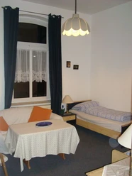 Bedroom Small, cozy living area corner with single bed, sofa, table and large window with dark curtains.