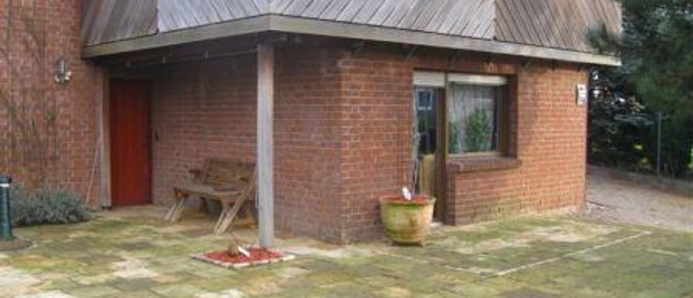 exterior view Een bakstenen huis met een groot raam, een houten balkon, een betegeld terras en een houten bank.