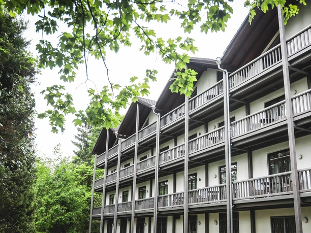 exterior view Een gebouw van meerdere verdiepingen met houten balkons, omgeven door groene loofbomen, onder een blauwe hemel.